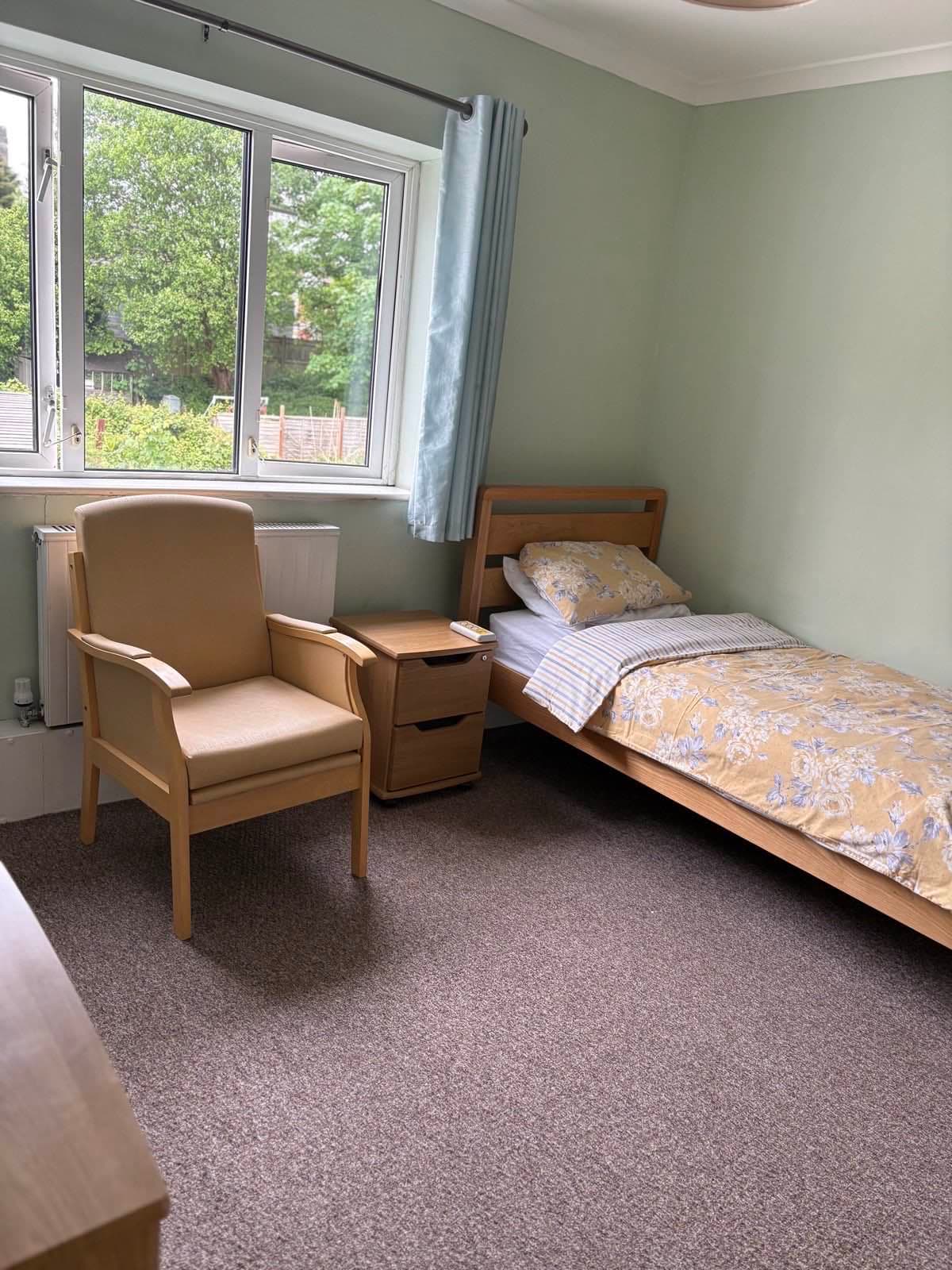 A single bedroom with sage-green walls, floral bedding and a window looking out to the garden.