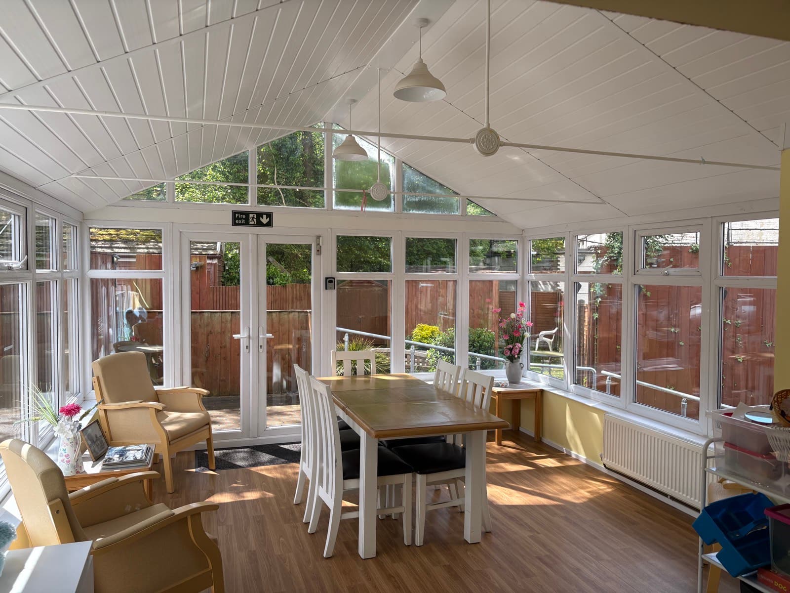 The conservatory in afternoon sun, with the dining table set and garden visible through the doors.