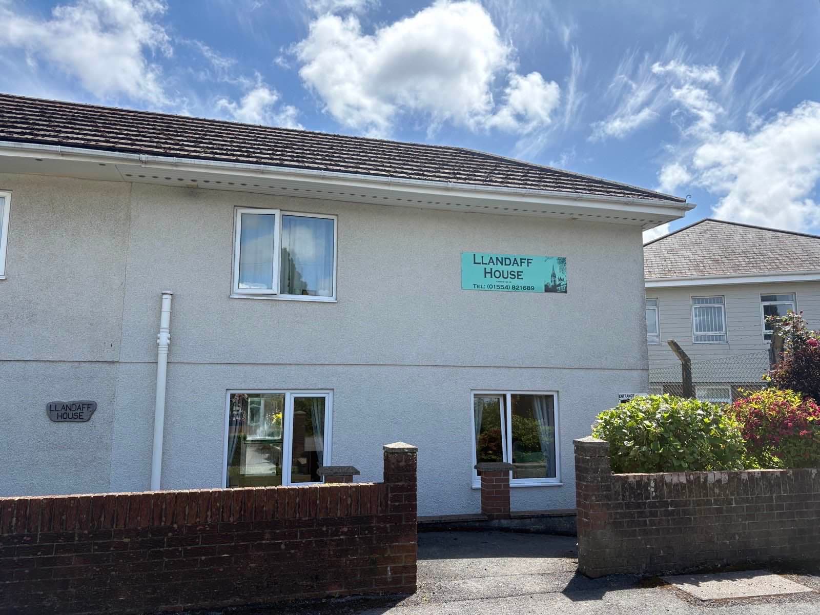 The front of Llandaff House on Mwrwg Road, with the teal sign and a blue summer sky.