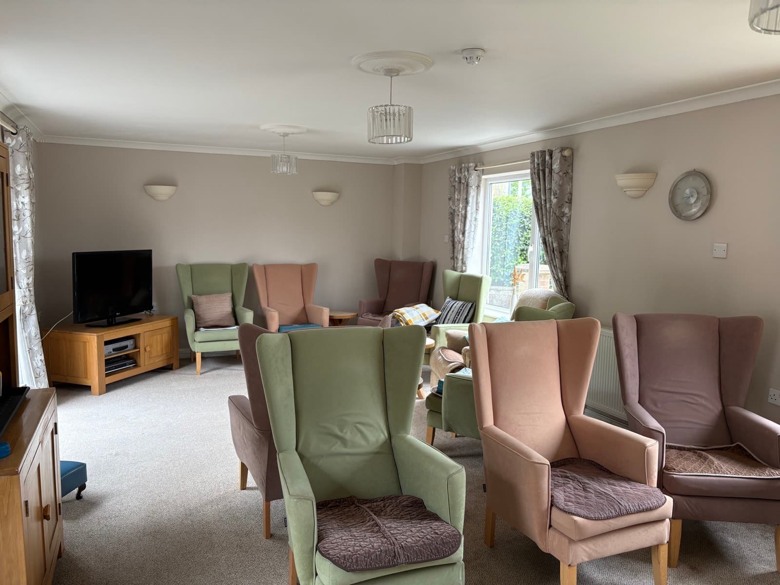 The main lounge, with sage and dusky-pink wingback chairs arranged around the TV.